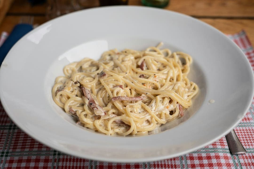Spaghetti carbonara in a white bowl on a checked tablecloth