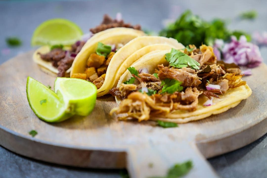 Three street tacos with lime wedges on a wooden board
